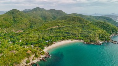 Nha Trang, Khanh Hoa, Vietnam 'daki Nhu Tien Sahili' nin havadan görünüşü turkuaz su, yemyeşil tepeler ve yumuşak kumlu kıyılarla dolu huzurlu bir gizli bölmeyi gösteriyor. El değmemiş orman ve küçük sahil kulübeleriyle çevrili bu sakin sahil,