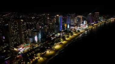 Vietnam, Khanh Hoa 'daki Nha Trang Sahili' nin çarpıcı hava manzarası, lüks sahil otelleri, altın kum, sakin mavi sular ve yemyeşil dağ sıraları ile canlı bir kıyı şehri manzarası sergiliyor. Akşam ışıkları kıyı şeridini aydınlatırken, şehir
