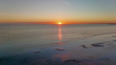 Bu hava görüntüsü, kumlu plajlar, sakin okyanus suları ve küçük bir sahil kasabasıyla çarpıcı bir sahneyi yakalar. Gün batımında çekilen altın ışık kıyı şeridini, kayalık kenarları ve kıyı yakınlarındaki evleri vurguluyor. Video.