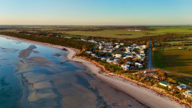 Bu hava görüntüsü, kumlu plajlar, sakin okyanus suları ve küçük bir sahil kasabasıyla çarpıcı bir sahneyi yakalar. Gün batımında çekilen altın ışık kıyı şeridini, kayalık kenarları ve kıyı yakınlarındaki evleri vurguluyor. Video.