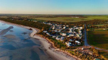 Bu hava görüntüsü, kumlu plajlar, sakin okyanus suları ve küçük bir sahil kasabasıyla çarpıcı bir sahneyi yakalar. Gün batımında çekilen altın ışık kıyı şeridini, kayalık kenarları ve kıyı yakınlarındaki evleri vurguluyor. Video.