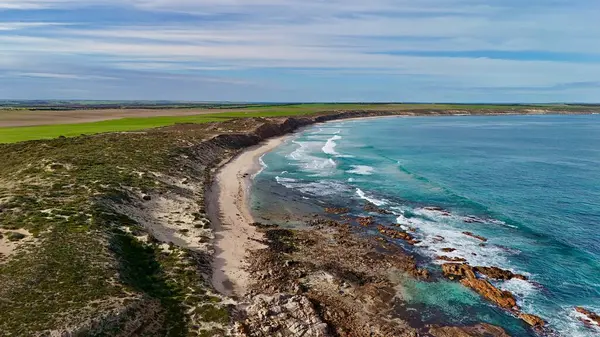 Bu hava görüntüsü Batı Sahili 'nin engebeli güzelliğini kayalık kıyılar, kayalık çıkıntılar ve kıyı boyunca dalgalanan turkuaz okyanus dalgalarıyla yakalıyor. Dokunulmamış doğal manzaralar ve açık tarım arazileriyle çevrelenmiş olan manzara, ham araziyi vurguluyor.