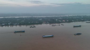 Bu büyüleyici 4K hava görüntüsü, Vietnam 'ın Mekong Deltası' ndaki My Tho City yakınlarında huzurlu bir nehir adasını gösteriyor. Tien Nehri 'nin geniş ve çamurlu sularıyla çevrili adada renkli evler, tekneler, palmiye ağaçları ve yeşil bitkiler bulunur.