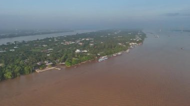 Bu büyüleyici 4K hava görüntüsü, Vietnam 'ın Mekong Deltası' ndaki My Tho City yakınlarında huzurlu bir nehir adasını gösteriyor. Tien Nehri 'nin geniş ve çamurlu sularıyla çevrili adada renkli evler, tekneler, palmiye ağaçları ve yeşil bitkiler bulunur.