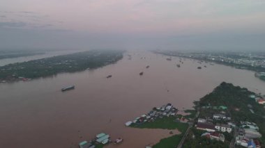 Bu büyüleyici 4K hava görüntüsü, Vietnam 'ın Mekong Deltası' ndaki My Tho City yakınlarında huzurlu bir nehir adasını gösteriyor. Tien Nehri 'nin geniş ve çamurlu sularıyla çevrili adada renkli evler, tekneler, palmiye ağaçları ve yeşil bitkiler bulunur.