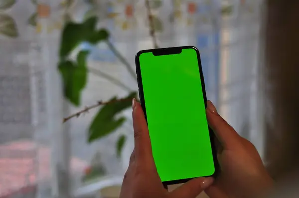 Kapalı alanda yeşil ekranlı akıllı telefonu tutan kadın eller.