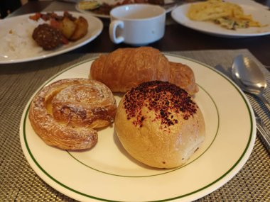 Kahvaltı büfesinde beyaz tabakta taze hamur işleri ve kruvasan.