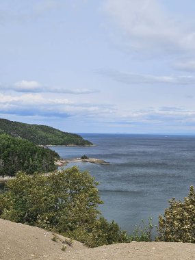 Kumlu kayalıkları, mavi okyanusu ve bulutlu bir gökyüzünün altında yemyeşil ormanı olan manzaralı bir sahil. Huzurlu körfez ve engebeli kıyı şeridi güzel bir doğal manzara yaratır. Seyahat, sahil manzarası, deniz manzarası ve açık hava macera temaları için mükemmel..