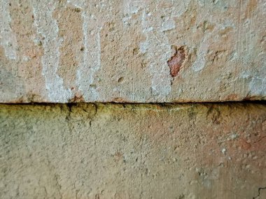 Yıpranmış bir duvar yüzeyinin yakın çekimi. Kabuk soyucu sıva, sert taşlar ve ince yosunlardan oluşuyor. Bu görüntü, kırsal ya da endüstriyel iç tasarım için ideal cazibe ve zengin doku taşır..