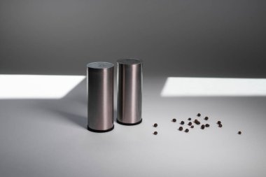 Metal biber karıştırıcı ve tuzluk, güneşten gelen ışıkla beyaz arka planda biber.