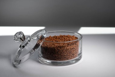 Gri arka planda cam bir kasede anlık kahve. Beyaz arka planda, gölgeli cam bir kavanozda kahve..