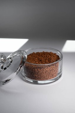 Gri arka planda cam bir kasede anlık kahve. Beyaz arka planda, gölgeli cam bir kavanozda kahve..