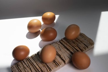 Tahtadaki tavuk yumurtaları, beyaz arka planda, güneşten gelen gölgelerle birlikte..