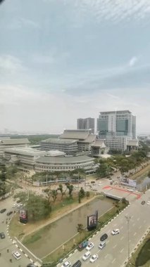 Şehir binalarının üst manzarası bir işyeri penceresinden görülüyor, aşağıdaki yolda trafik sorunsuz akıyor, kentsel sakinliği ve günlük rutini yakalıyor.