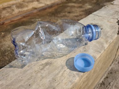 Kapağı açık ezilmiş plastik bir şişenin yakın çekimi, atıkları, kirliliği ve tek kullanımlık ambalajın çevre üzerindeki etkisini simgeliyor..