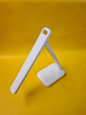 Plastik malzemeden yapılmış beyaz çalışma lambası, basit ve işlevsel bir yapıya sahip masa kullanımı için tasarlanmış..
