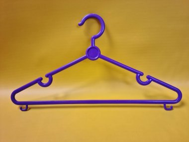 Mor plastik bir askı parlak sarı bir zemin üzerinde belirgin bir şekilde sergilenir, şekli ve renk kontrastı vurgulanır.