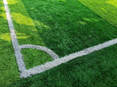 Yeşil çimen sahasında köşe tekme izi, beyaz dairesel nokta ve çim dokusunu gündüz vakti futbol sahasının bir parçası olarak gösteriyor..