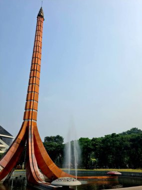 Bir parkta, etrafında fıskiyeler olan heykel dikiliyor. Mimari, su özellikleri ve yeşil manzarayı birleştiren popüler turistik cazibe.