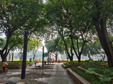 Jakarta, Endonezya - 27 Haziran 2025: Yeşillik, kültür pavyonları ve gezgin park yollarında gezinen ziyaretçilerin yer aldığı TMII manzarası.