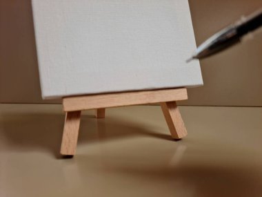 Ahşap sehpanın üzerindeki boş tuval, yanında kalem, yaratıcılığı, fikirleri ve sanatsal ifadeyi sembolize ediyor..