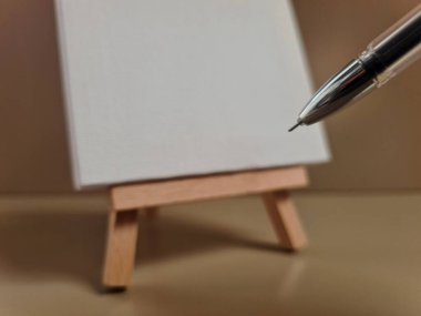 Ahşap sehpanın üzerindeki boş tuval, yanında kalem, yaratıcılığı, fikirleri ve sanatsal ifadeyi sembolize ediyor..