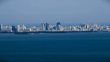 Da Nang, Vietnam 'ın uzak ufuk çizgisi görüntüsü, Haziran 2025' te telefon lensiyle deniz aşırı bir yerde çekilmiş. Sahil ufku boyunca açık mavi gökyüzü altında modern yüksek binalar..