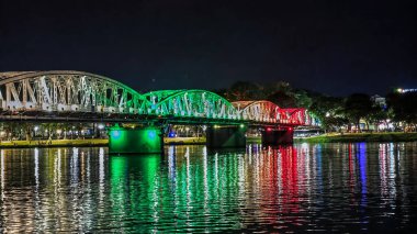 Hue, Vietnam 'daki Truong Tien Köprüsü' nün gece görüşü. Köprü renkli ışıklarla aydınlanıyor, Parfüm Nehri 'ne yansıyor, canlı ve manzaralı bir şehir manzarası yaratıyor.