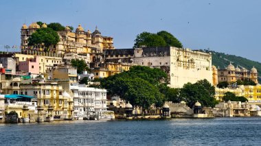 Udaipur 'daki Şehir Sarayı kompleksinin görkemli manzarası Pichola Gölü' nün sakin sularını yansıtıyor. Açık bir yaz günü, Rajasthan, Hindistan, Ağustos 2025.