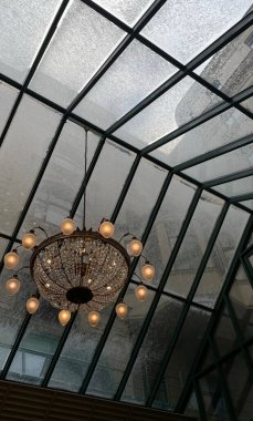 Taze karla kaplanmış çelik çerçeveli çatı penceresinin altında sıcacık parlayan süslü kristal avizenin yukarıdan görünüşü, ışıl ışıl iç zarafetle soğuk hava arasında çarpıcı bir kontrastlık yaratır.