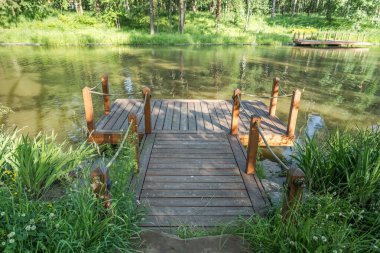 Berrak bir ahşap iskele, bereketli yeşillik ve sakin sularla çevrili sakin bir gölet ile zarifçe uzanır.