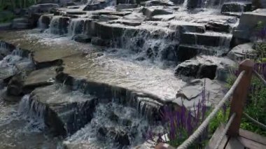 Şaşırtıcı derecede güzel bir şelale zarif bir şekilde akmakta, yemyeşil ve canlı çiçeklerle sarılmış kayalardan aşağı yuvarlanmaktadır.