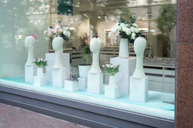 Şık ve modaya uygun bir mağaza penceresi zarif minimalist vitrinlerde şık çiçek düzenlemeleri sergiliyor.