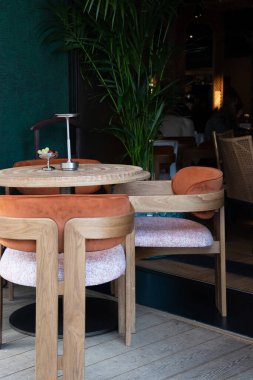 Bu şık yemek alanında güzel ahşap mobilyalar sergileniyor. Canlı turuncu yastıklar ve gür yeşillikler eşleştiriliyor.