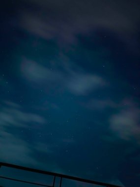 Yıldızlarla dolu bir gece gökyüzünün güzel bir görüntüsü. Tırabzanın üzerinde bir ışık bulutu var. Huzurlu ama modern bir gece ortamını ön plana çıkarıyor..