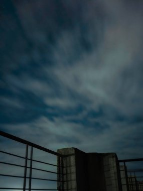 Yumuşak, bulanık bulutlar ve soluk yıldızlarla dolu, sakin, gizemli bir şehir atmosferini çağrıştıran, gece gökyüzünün altında bir çatı..
