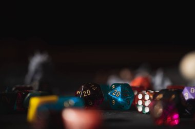 Siyah bir yüzey üzerinde renkli RPG zar koleksiyonu. Üzerinde mavi bir D20 var. Kompozisyon, üstte büyük, koyu kopya alanı bırakıyor, afişler veya web sitesi başlıkları için ideal.