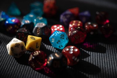 Canlı bir mavi D20 zarı, renkli bir RPG zar koleksiyonunun merkezinde yer alır. Görüntü, Zindanlar ve Ejderhalar gibi masa üstü oyunlarında çok önemli bir şansı simgeliyor..