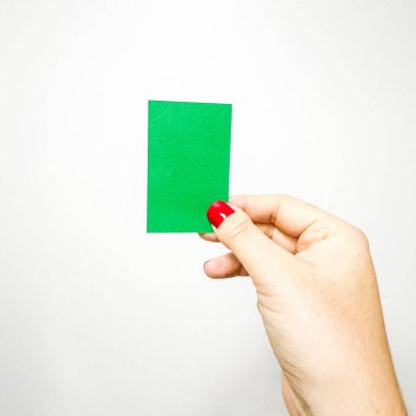 Açık tenli bir el beyaz arka planda dikdörtgen şeklinde bir yeşil kart tutar. Başparmak D tipi brachydactyly gösteriyor, ve çivi kırmızı..