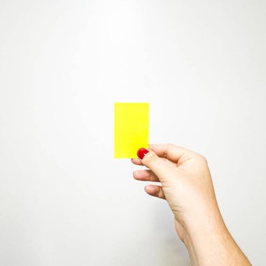 Açık tenli bir el ve kol beyaz bir arkaplana karşı dikdörtgen sarı bir kart tutuyor. Başparmak D tipi brachydactyly gösteriyor, ve tırnak kırmızıya boyanmış..