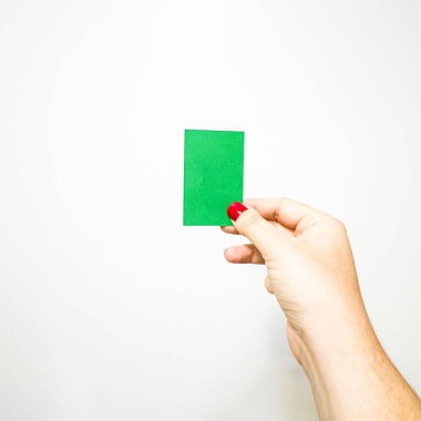 Açık tenli bir el ve kol, beyaz bir arka plana karşı dikdörtgen şeklinde yeşil bir kart tutuyor. Başparmak D tipi brachydactyly sergiler, ve çivi kırmızı.