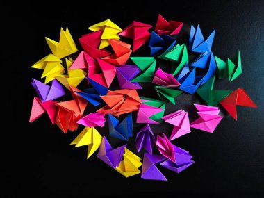 Artwork in colored paper with geometric shapes on a black background. Colors: blue, green, pink, purple, orange, yellow, red.