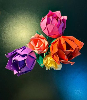 Siyah bir ofis masasındaki vazoda beş kağıttan çiçeğin üst görüntüsü. Renkler: mor, açık pembe, koyu pembe, sarı ve turuncu.