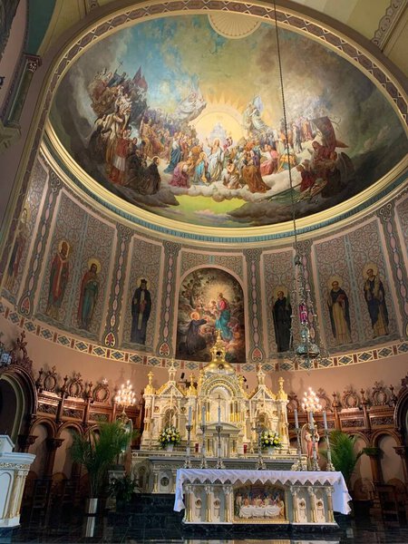 Interior view of a Catholic church featuring a gold-adorned altar, painted religious images, and rows of candles
