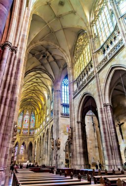 Uzun kemerler, karmaşık vitray pencereler ve ahşap sıralardan oluşan büyük bir katedralin iç manzarası. Işık pencerelerden süzülerek sakin bir atmosfer yaratıyor..