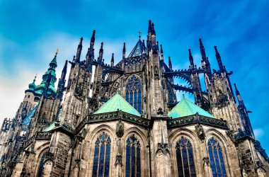 Parlak mavi gökyüzüne karşı sivri kuleleri ve yeşil bakır çatıları olan, karmaşık mimarisi olan gotik bir katedralin çarpıcı manzarası..