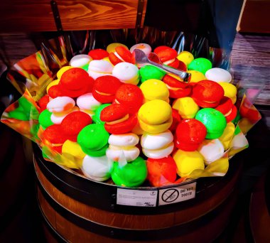 Tahta bir fıçıda sergilenen renkli bir banyo bombası çeşidi. Banyo bombaları kırmızı, sarı, yeşil ve beyaz gibi canlı renklerde. Görsel olarak çekici bir şekilde düzenlenmiş..