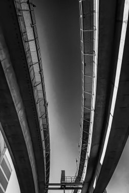 Yüksek beton yapıların karmaşık kıvrımlarını gösteren dramatik siyah beyaz bir fotoğraf. Görüntü, mimari tasarımı vurgulayarak ışık ve gölgenin etkileşimini yakalar..