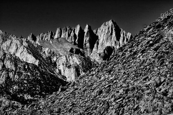 A dramatic black and white landscape featuring rugged mountain peaks and rocky terrain.