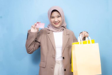 Mutlu Asyalı Müslüman kadın alışveriş torbaları tutuyor ve pembe arka planda izole edilmiş iyi niyet göstergesi gösteriyor.